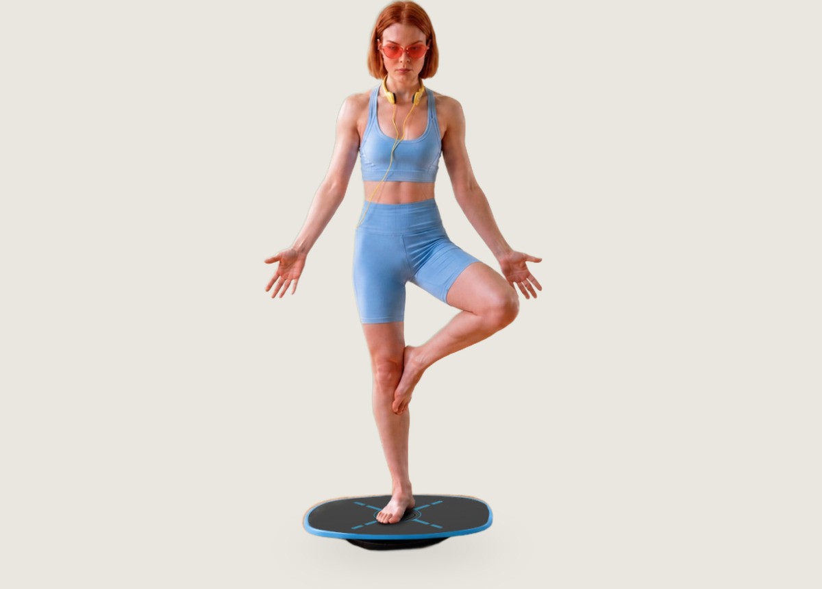 A woman holding a one-leg balance on the GoBalance Sport board